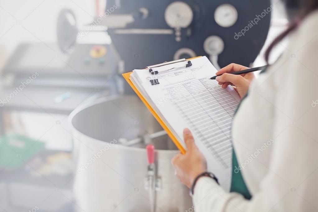 Koenig Food Safety specialist filling out a GMP audit checklist next to mixing equipment in an infant formula processing plant.
