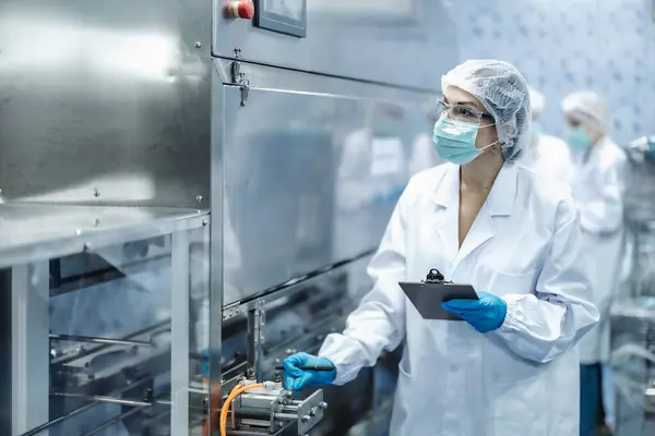 depositphotos_801870196-stock-photo-industry-inspector-team-working-staff Technician wearing full PPE and holding clipboard, inspecting sterile packaging machinery for infant formula in a cleanroom environment.