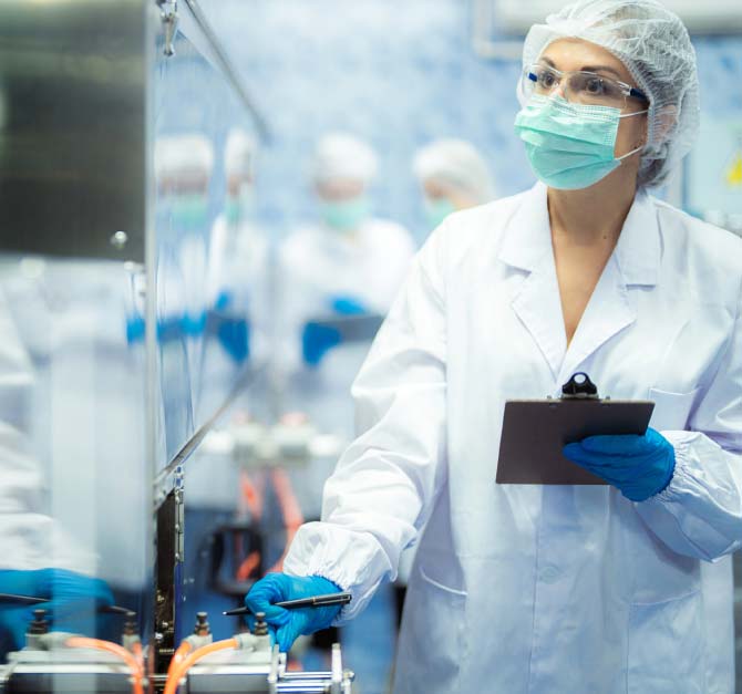 sqf-certification-program Female quality assurance specialist in a white lab coat and safety gear performing a manual SQF certification gap assessment and documentation review on a food production line