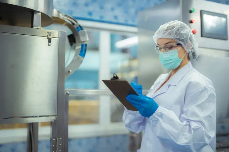 Quality assurance inspector reviewing equipment and documenting findings during a food safety GMP audit